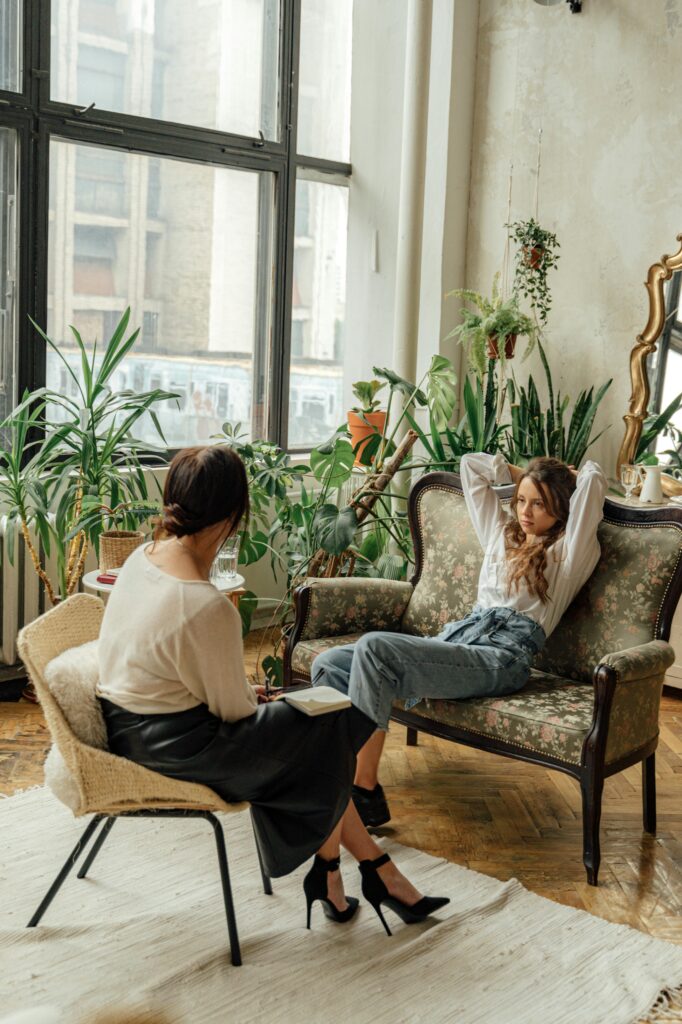 Two women engaged in a counseling session in a cozy, plant-filled living room.