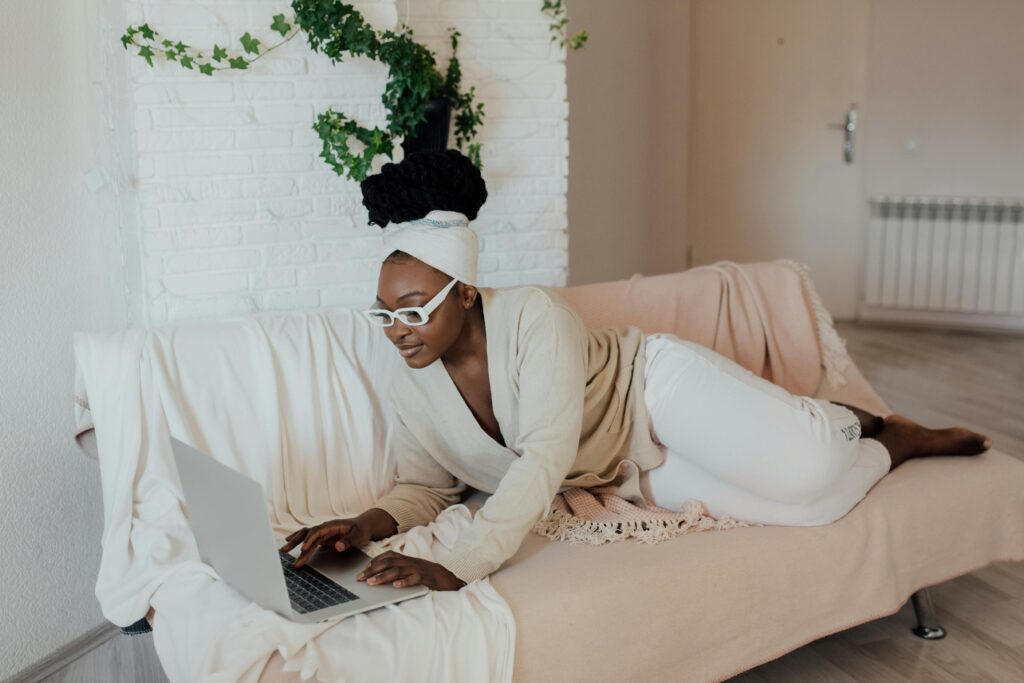 Woman in glasses working from home on a cozy couch with a laptop, creating a comfortable lifestyle scene.